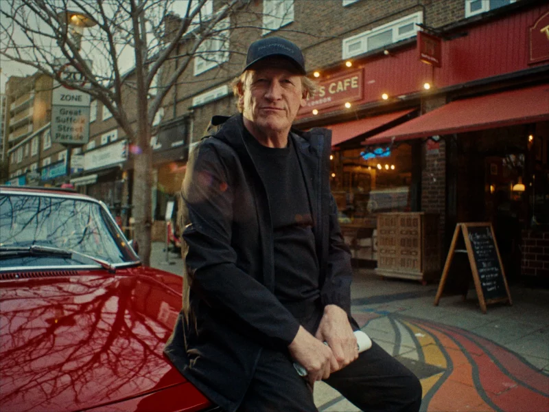 Actor Geoff Bell sitting on the bonnet of a vintage sports car outside Terry's Cafe.